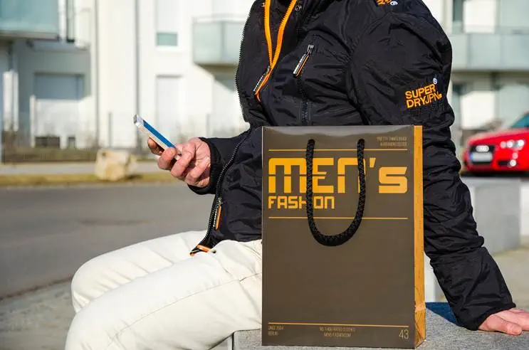 Schwarze orange Papiertragetasche vor einer sitzenden Person